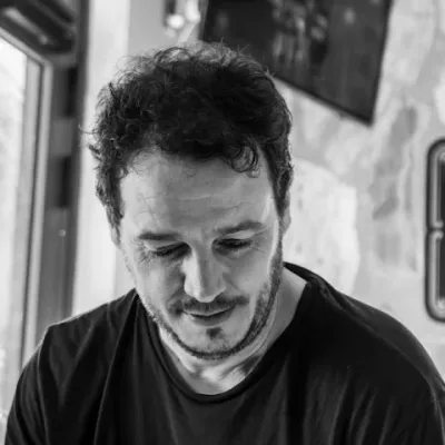Retrato en blanco y negro de Esteban de Aymerich, con la mirada baja, camiseta oscura y una pared de piedra al fondo.