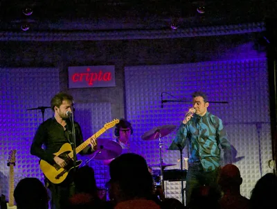 David y el guitarrista cantan a la vez, cada uno en su micrófono, con luz morada.