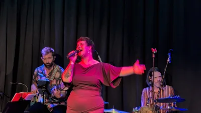 Cantante con vestido malva abriendo el brazo hacia un lado, con luz roja.