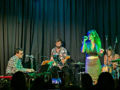La cantante de falda de lentejuelas junto al teclista y al guitarrista, con luz verde.
