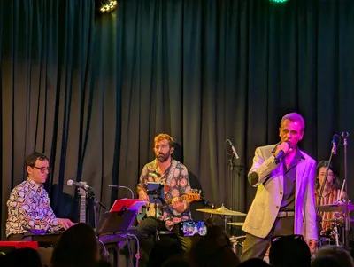 Cantante con traje gris cantando junto al teclista, con la banda detrás.