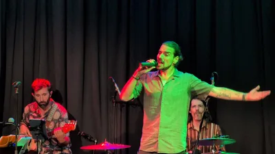 Cantante con coleta y camisa verde abriendo los brazos, iluminado en verde.