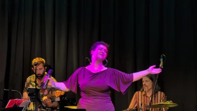 La cantante de vestido malva con los brazos abiertos y una sonrisa.