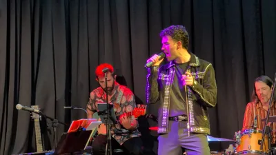 Cantante joven con chaqueta negra de tachuelas, cantando de frente.