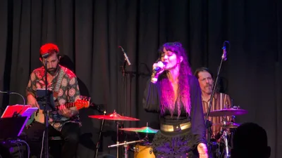 Cantante de melena larga y vestido oscuro con falda de lentejuelas, bajo luz morada.