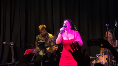 Cantante con vestido rojo ajustado, con manos y móviles del público en primer término.