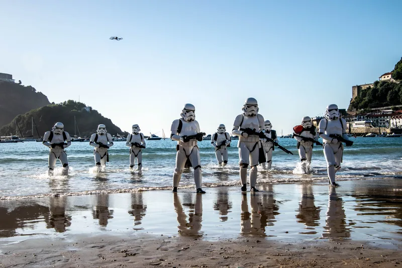 Star Warseko soldadu inperialen ilara bat uretatik Kontxako ertzera ateratzen da, harea bustian islatuta; atzean, Igeldo, uhartea eta drone bat.