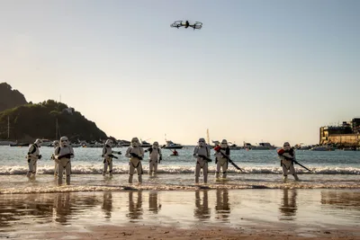 Una línea de soldados imperiales sale del agua al atardecer, con Igeldo y la isla de Santa Clara detrás y un dron sobre ellos.