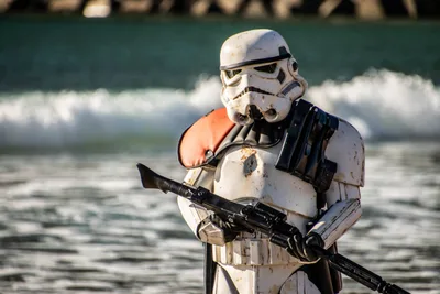 Soldado imperial de armadura desgastada y hombrera naranja, con el fusil cruzado, delante de una ola que rompe.