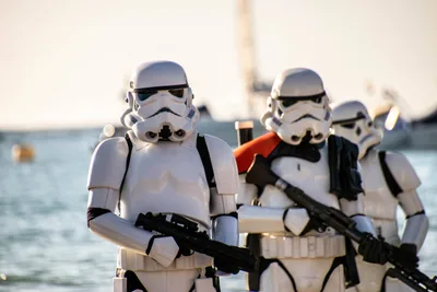 Tres soldados imperiales en fila, el del centro con hombrera roja, con las armas en las manos y la bahía detrás.
