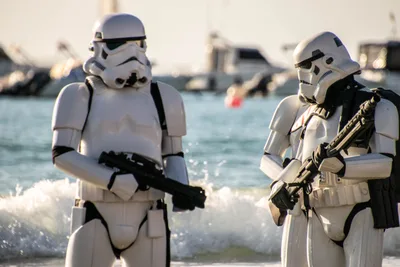 Dos soldados imperiales en la orilla, uno con un fusil cruzado, con la espuma de las olas a sus pies.