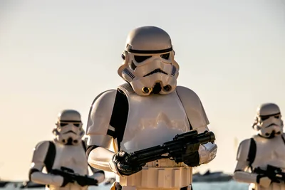 Soldado imperial con el fusil en las manos y dos compañeros desenfocados a los lados, con el cielo claro de la tarde.