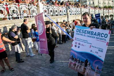 Una oficial imperial con un sable de luz y un voluntario con el cartel «Desembarco contra el cáncer infantil, a favor de Aspanogi, Playa de La Concha, 18:00».