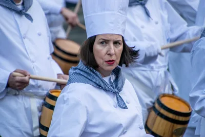Una cocinera con pañuelo de cuadros azules toca la barrica entre otros cocineros.