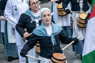 Una aguadora con cofia blanca, chaqueta azul marino y toquilla celeste toca la barrica.
