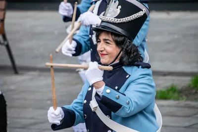 Una tamborrera de azul celeste y guantes blancos toca con las baquetas cruzadas.