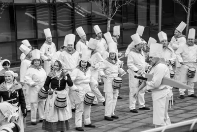 En blanco y negro, las filas de cocineros con gorro alto tocan sus barricas.