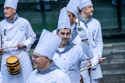 Cocineros sonrientes con barricas; uno levanta las baquetas.
