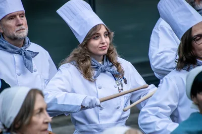 Una cocinera joven de pelo largo, con gorro alto, toca con las baquetas.