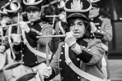 En blanco y negro, una tamborrera sujeta las baquetas cruzadas delante de la cara.