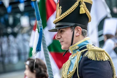 El tambor mayor de perfil, con charreteras doradas y chacó con cordones, junto a la ikurriña.