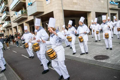 Los cocineros desfilan por la calle tocando, con los portales del barrio detrás.