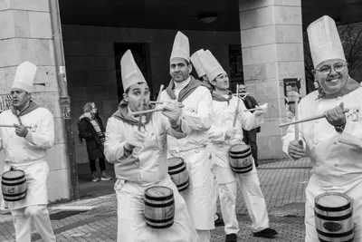 En blanco y negro, cocineros sonrientes tocan las barricas mientras avanzan.