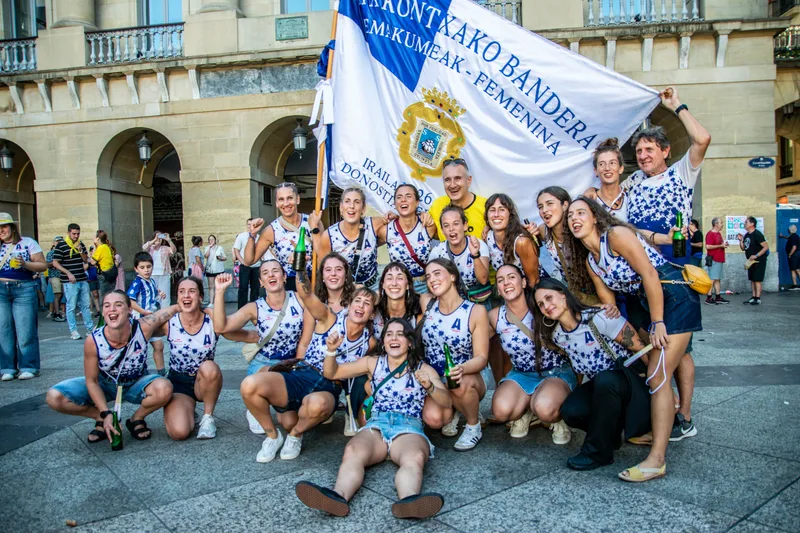 La tripulación de Arraun Lagunak, agachada y de pie, posa en la plaza delante de la Bandera de La Concha femenina.