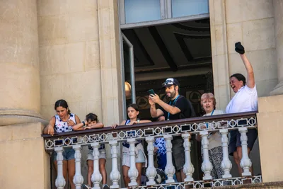 En un balcón lateral, niñas con la camiseta del club y un hombre que saluda con la gorra en alto.