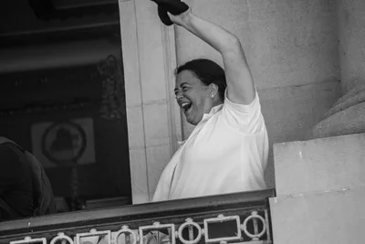 En blanco y negro, una mujer se ríe y agita una gorra desde una ventana del ayuntamiento antiguo.