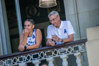 Una remera y un hombre mayor de polo blanco, copa en mano, apoyados en la barandilla.