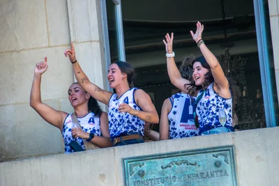 Tres remeras levantan los brazos en el balcón, sobre la placa de la plaza.