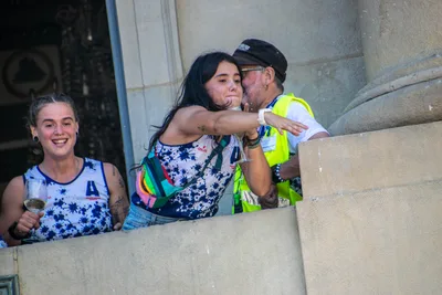 Una remera abraza y besa a un hombre con chaleco amarillo en el balcón, y otra sonríe al lado.