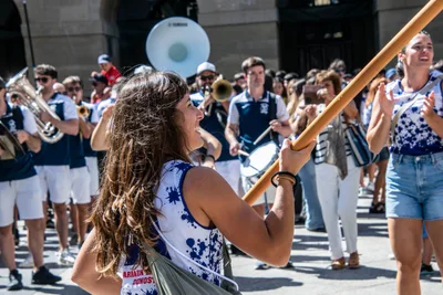 Una remera baila con el asta de la bandera delante de una banda de música.