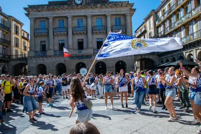 La Bandera de La Concha ondea en medio de la plaza llena, con el antiguo ayuntamiento detrás.