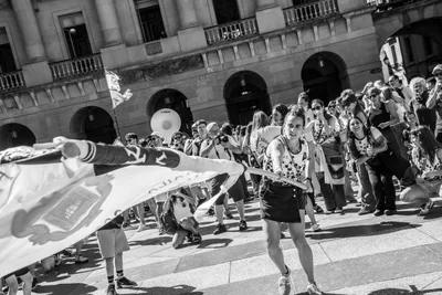 En blanco y negro, la bandera pasa a ras de suelo entre la gente de la plaza.
