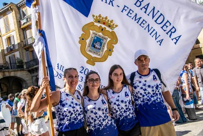 Cuatro remeras y un hombre posan con la bandera y el escudo de Donostia detrás.