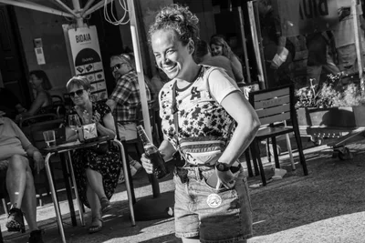 En blanco y negro, una remera se ríe con una botella en la mano delante de una terraza.