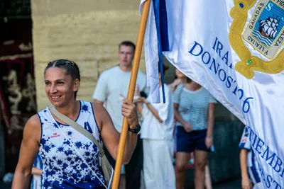 Una remera sonriente sujeta el asta de la bandera, que le cae por el lado.