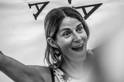 En blanco y negro, una mujer con cara de asombro y la boca abierta bajo la bandera.