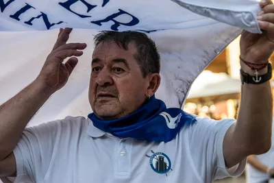 Un hombre con pañuelo azul al cuello sostiene la bandera por encima de la cabeza.