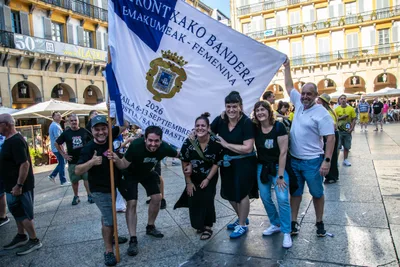 Un grupo vestido de negro posa con la bandera extendida en la plaza.