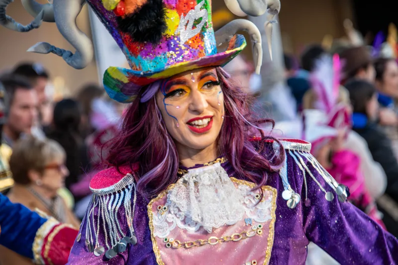Mujer con chistera de colores y casaca morada, con la cara pintada de purpurina, entre el público.