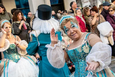 Comparsa de época: vestidos azules de faralaes, chistera y gorguera blanca.