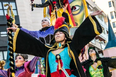Un bailarín con casaca negra y dorada y bicornio abre los brazos delante de una carroza.
