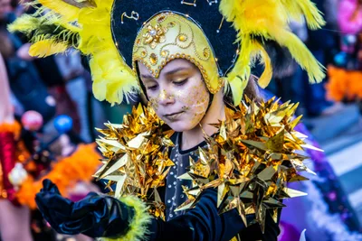 Joven con tocado dorado de plumas y hombreras de estrellas doradas, con guantes negros.