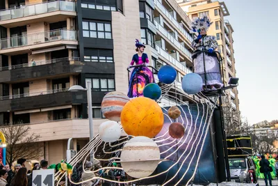 Carroza del sistema solar, con planetas de colores colgando, entre los bloques de viviendas.