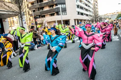 Comparsa de monos ceñidos azules, rosas y verdes bajando la calle en formación.