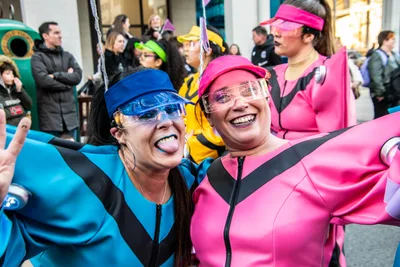 Dos mujeres con monos azul y rosa y gafas de visera, riendo abrazadas.
