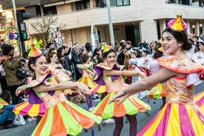 Comparsa con faldas de colores y gorros cónicos, bailando cogidas de la mano.